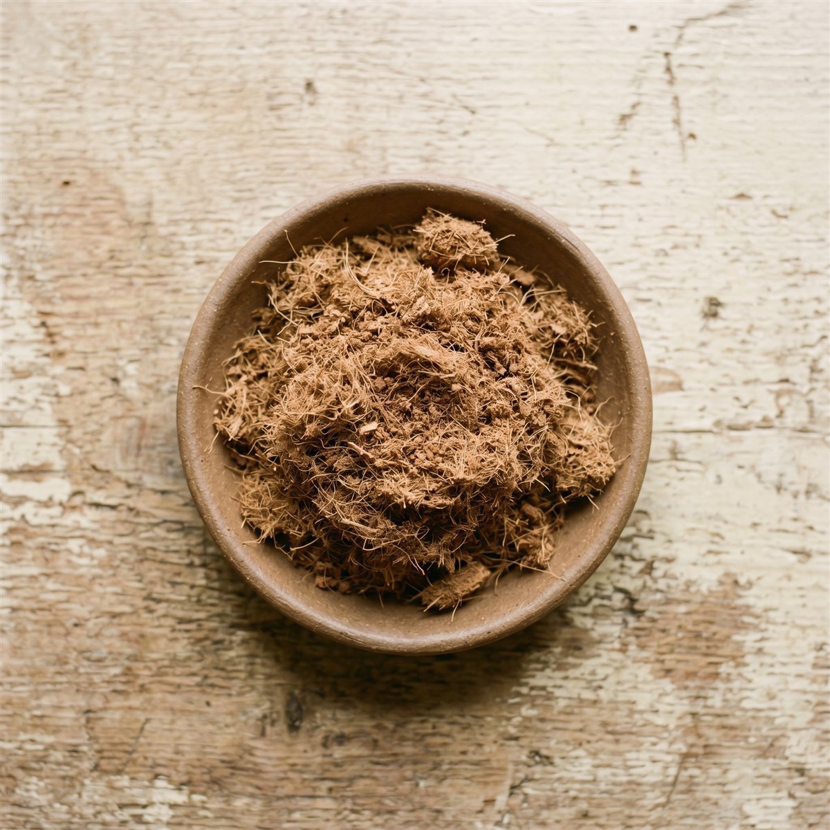 Buffered coconut coir in a ceramic bowl on a weathered wood surface